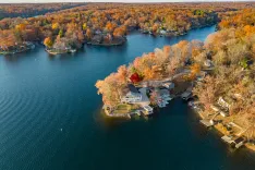 Aerial view of a lakeside residential area with colorful autumn trees and houses with boat docks during the fall season.
