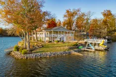 A serene lakeside home with autumn foliage, featuring a waterslide and private dock under a clear sky.