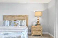A cozy bedroom with a distressed wooden headboard, bed with striped blue and white bedding, a decorative anchor pillow, and a nightstand with a lamp.