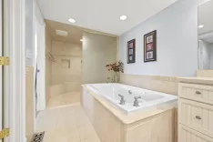 Elegant bathroom interior with large built-in bathtub, walk-in shower area, beige tiling, and vanity cabinet with rectangular mirror and decorative framed pictures on the wall.