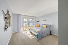 Bright, nautically themed bedroom with a view of the water through large sliding glass doors, decorated with ocean-inspired ornaments and a 'Ahoy' sign above the bed.