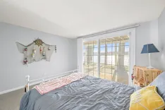 Cozy bedroom interior with nautical decor, a queen-size bed, a seaside view through the glass door, and soft natural lighting.