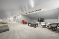 Spacious, modern attic living area with slanted ceilings, track lighting, a sectional sofa, eclectic furniture, a flat-screen TV, and neutral color scheme.