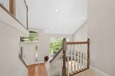 Bright interior view of a home's landing area with wooden stair railing, high ceiling, and front door with sidelights.