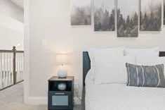 Cozy bedroom interior with a white bedding set, a small bedside table with a lamp, and framed pictures of trees on the wall.