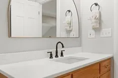 A clean and modern bathroom vanity with white marble countertop, undermount sink with dark fixtures, and framed mirror above, flanked by white towels hanging on black circular towel holders.