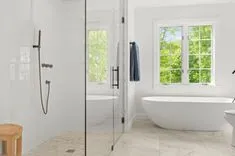 Bright modern bathroom with a walk-in shower, freestanding bathtub, wooden stool, and window showing green foliage outside.