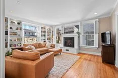 Bright and cozy living room with leather sofas, hardwood floors, fireplace, built-in bookshelves, and large windows.
