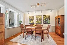 Bright dining room with wooden table and chairs, hardwood floors, white area rug, and artwork on the walls.