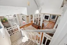 Overhead view of a multi-level home interior with white railing, wood flooring, and a glimpse into the living areas.