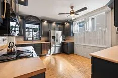 Modern kitchen interior with stainless steel appliances, black countertops, white cabinetry, and hardwood floors.