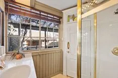 Brightly lit bathroom interior with a claw-foot tub, shower stall, wooden window blinds, and a decorative plant on the windowsill.