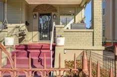 Front porch of a suburban home with pink steps, a red railing, and a decorative glass front door.
