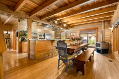 Spacious wooden cabin interior with modern kitchen appliances, a long dining table with chairs, and a wood-burning stove.