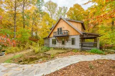 A rustic wooden cabin with a balcony surrounded by autumn foliage in a forest setting.