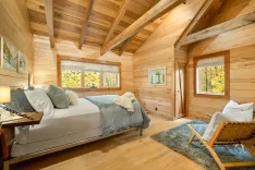 Cozy wooden cabin bedroom with a large bed, natural light, and a view of trees through the windows.