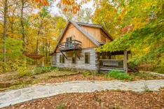 Rustic wooden cabin surrounded by autumn foliage with a stone pathway leading to the entrance.