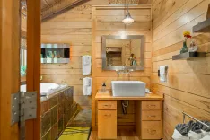 Cozy wooden bathroom interior with a standalone sink, mirror, bathtub, and towels on display.