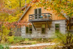A cozy wooden cabin with a balcony surrounded by autumn foliage.