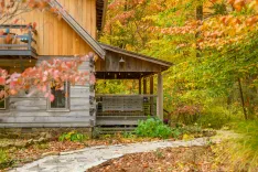 Rustic wooden cabin with a covered porch surrounded by autumn foliage in a serene forest setting.
