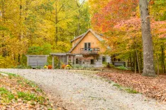 Cozy wooden cabin surrounded by autumn foliage with fallen leaves on the ground and seasonal decorations near the porch.