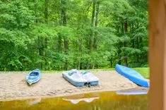 Kayaks and a paddle boat on a sandy lakeshore with lush green trees in the background.