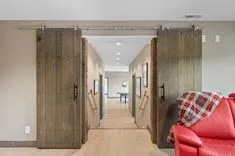 Rustic barn-style sliding doors open to a modern hallway with wood flooring and a partial view of a red leather couch with a plaid throw blanket.