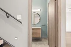 Modern bathroom interior with wooden elements, a round mirror, and sleek design visible through an open door.