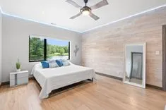 Modern bedroom with a wooden accent wall, large window overlooking a green landscape, LED ceiling lighting, and a minimalistic design.