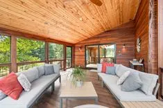 Bright and airy wooden interior of a modern cabin with large windows, comfortable seating, and a view of greenery outdoors.