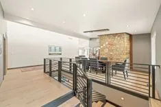 Modern open concept living space with wooden floors, stone accent wall, and metal railing leading to a lower level.