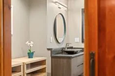 Modern bathroom interior with floating vanity cabinet, vessel sink, large round mirror, and decorative plant.