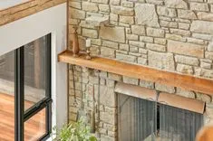 Stone fireplace with a wooden mantel decorated with a copper vase and candles, next to a modern window.