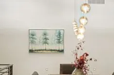 Elegant living room with a framed painting of trees on the wall, a modern chandelier and blurred flowers in the foreground.