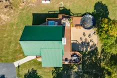 Aerial view of a residential backyard with a trampoline, hot tub, patio, and outdoor seating area surrounded by trees.
