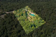 Aerial view of a forested area with a clearing containing buildings and a small pond.