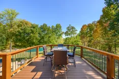 Spacious wooden deck with patio furniture overlooking a forested backyard on a sunny day.