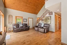Spacious living room with vaulted wooden ceiling, leather sofas, hardwood floors, and staircase.