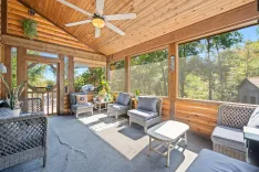 Sunny screened porch with wicker furniture, ceiling fan, and verdant forest view.