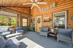 Cozy wooden cabin porch furnished with comfortable seating, decorative plants, and a "HAPPY PLACE" sign on the door.