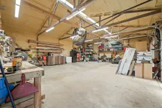 Spacious, well-organized workshop with various tools and materials, lit by fluorescent lights with a concrete floor.