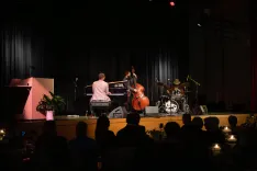 Jazz musicians performing on stage with piano, double bass, and drums in front of an audience.