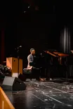 Person playing a grand piano on a dimly lit stage.