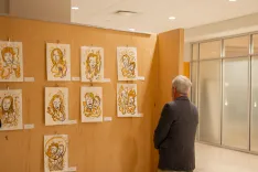 A person viewing an art exhibition with multiple framed drawings on display.