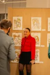 Person smiling and posing in front of artwork at a gallery exhibition while someone else with their back turned is in the foreground.