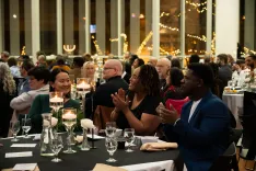 Guests seated at tables applauding at an indoor gala event.