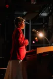 Person giving a speech at a lectern on a dimly lit stage.