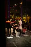 Woman playing piano on stage under spotlight.