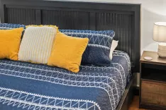 A neatly made bed with blue and white bedding and multiple pillows, featuring a black headboard and a bedside table with a lamp.