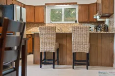 Modern kitchen interior with wooden cabinets, two wicker bar stools, and a window with blinds.